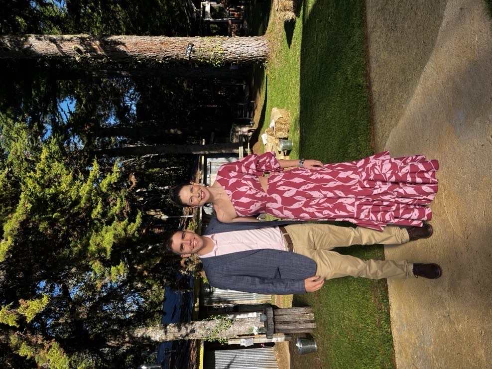 Stefy y Joaco sonriendo en un jardín, ella con vestido floreado rosa y él con chaleco y camisa